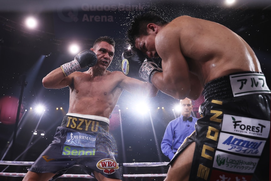 A spray of water comes from a Japanese boxer covering up as his Australian opponent lands with a left.