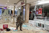 A soldier walks through a damaged mall with debris littered across the fall.