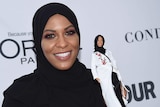 Glamourous woman wearing hijab holds barbie doll also wearing hijab.