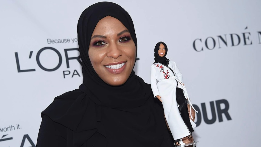 Glamourous woman wearing hijab holds barbie doll also wearing hijab.