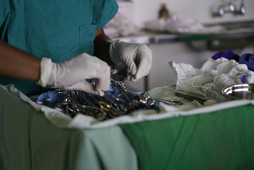 A close-up shows gloved hands preparing surgical equipment on a tray