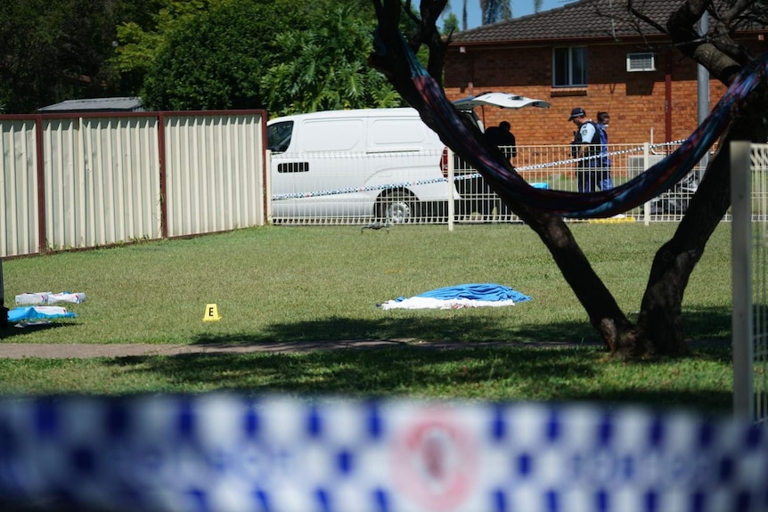 Sheets are seen lying on the ground of a yard, with police seen near a house.