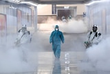 Volunteers in protective suits disinfect a railway station as steam fills the air.