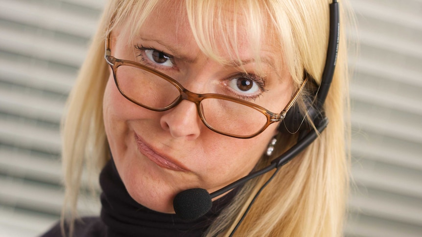 woman with blonde hair and glasses wearing a telephone headset has a puzzled look on her face