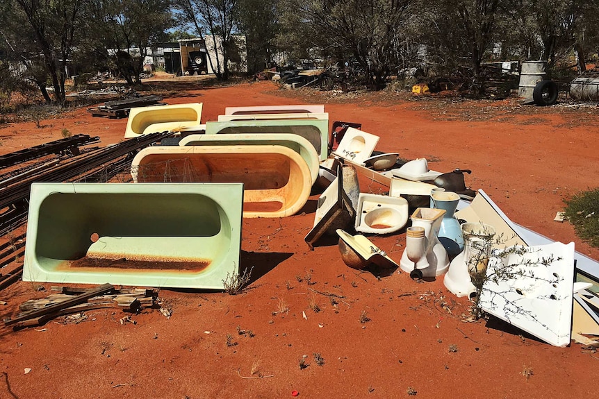 A collection of old baths sits propped up in red dirt.