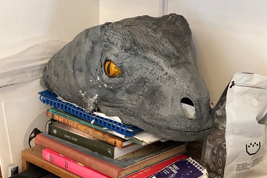 A Styrofoam model of a raptor dinosaur head sits on a bookshelf