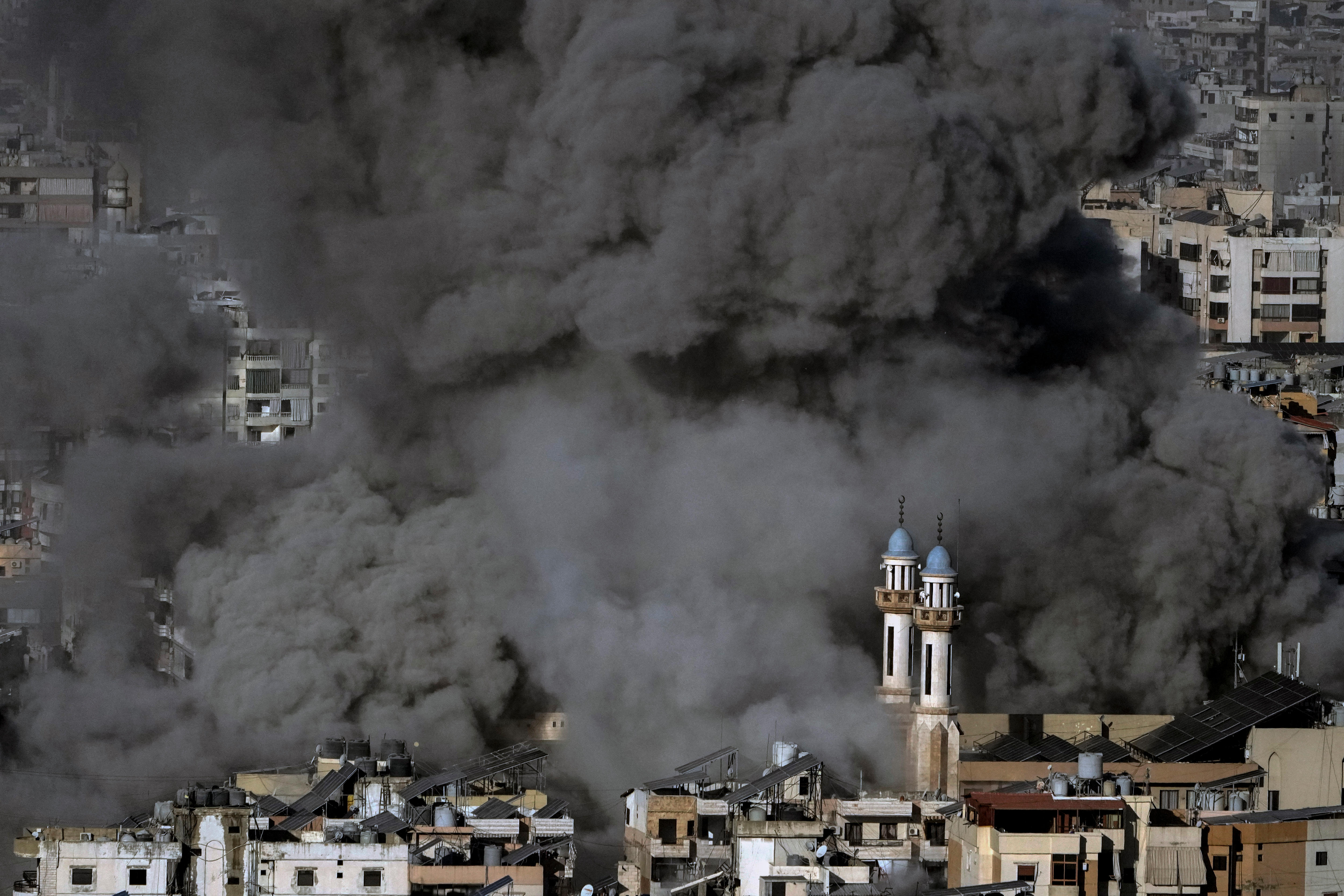 The tops of Lebanese homes and churches almost entirely obscured by thick grey and black smoke plumes