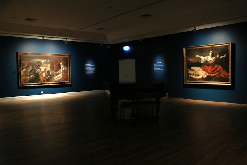 A large, dimly lit gallery space with large historic paintings on walls