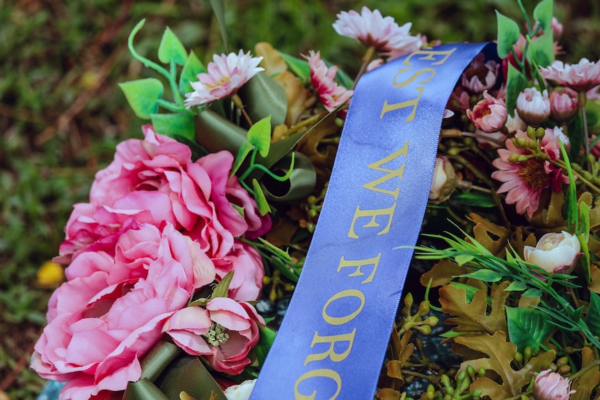 A flower wreath with a 'lest we forget' sash laid across it. 