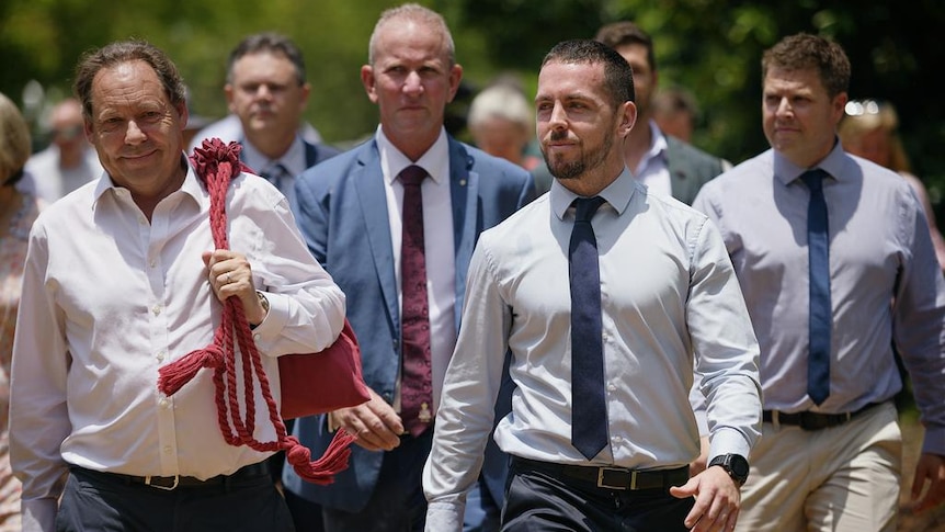 Zachary Rolfe walking out of a court with a group of supporters, as one pats him on the back.