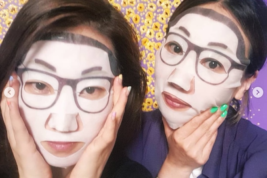 Two women wear the Kim Jong-un face masks, which have glasses and a strong hairline.