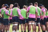 Rugby union players huddle in a circle listening to their captain talk