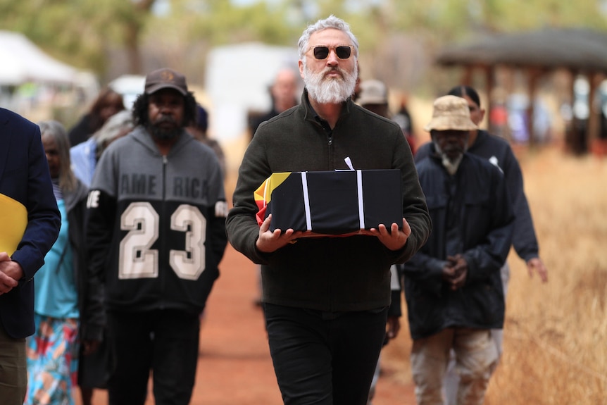 A man carries a box draped in the Aboriginal flag.