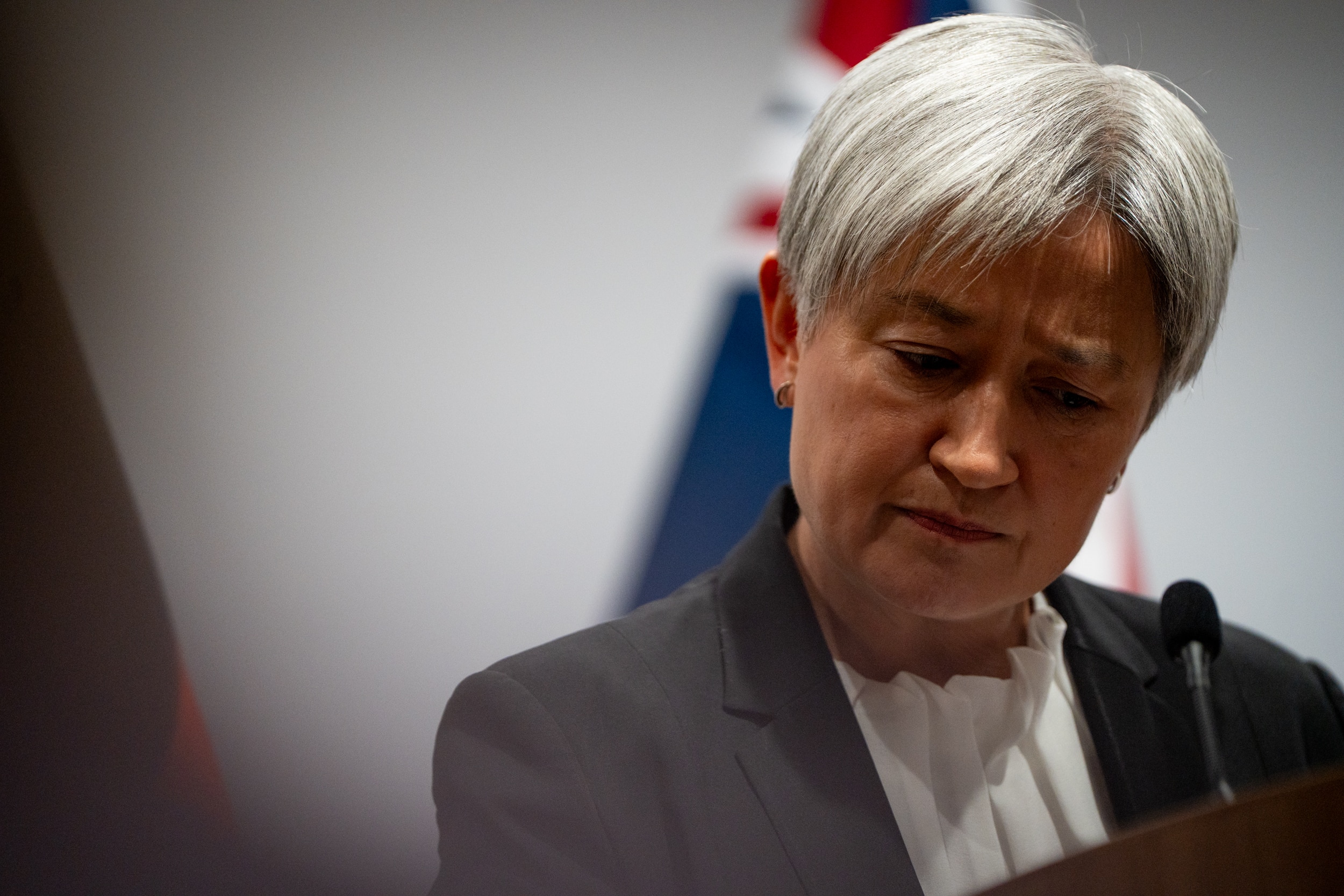 Penny Wong dips her head, looking downward. Behind her is an Australian flag.