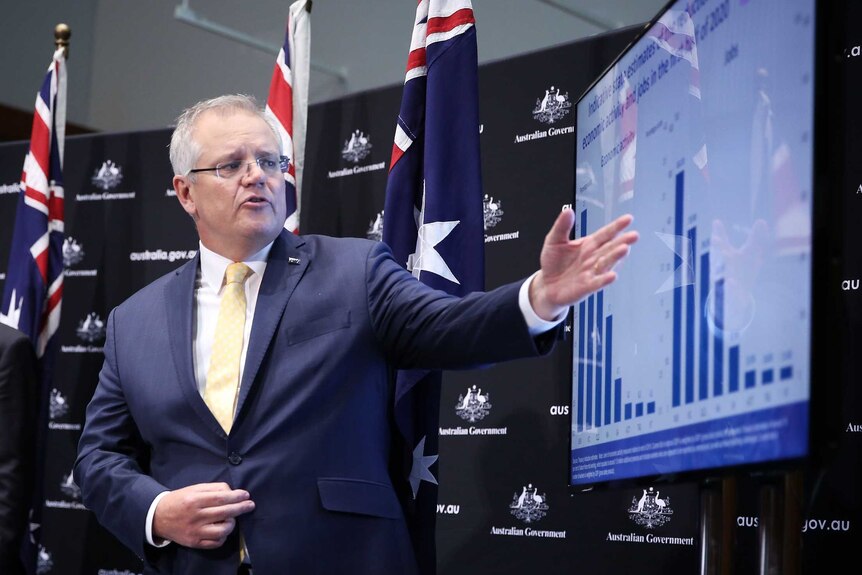 Prime Minister Scott Morrison gestures to a screen with a chart on it.