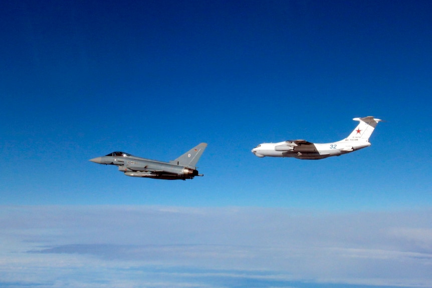 A silver-grey fighter jet leads a bulbous, white-grey refuelling tanker aircraft in front of a blue sky.