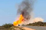 On a desert highway in the distance a large flame towers over a truck cabin