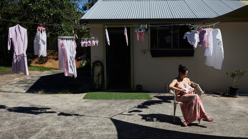 A woman sits topless in a concrete courtyard reading.