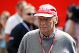 An old man stands with a cap on his head and a lanyard around his neck before Formula One practice.