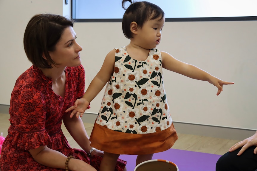 A young girl points off camera, with her mum watching her closely.