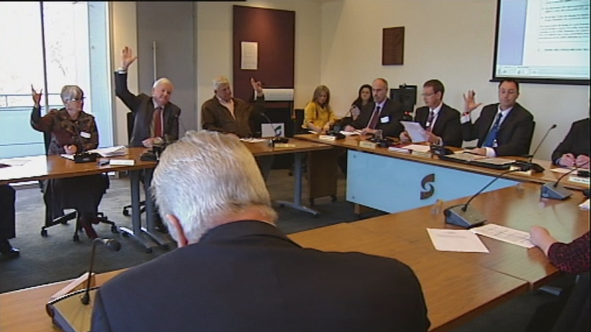 A group of people raise their hands at a table during a meeting