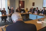 A group of people raise their hands at a table during a meeting