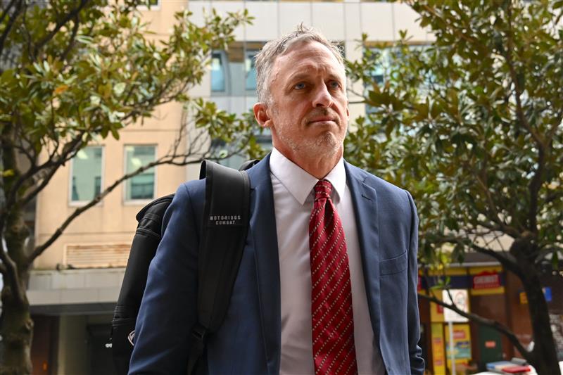 Titus Day, el ex gerente de la estrella del pop australiana Sebastian, usa un traje azul con una camisa blanca y una corbata roja.