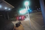 A police officer has his gun drawn at a car on a footpath