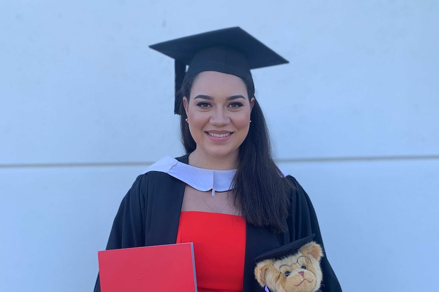 Graduation photo of Melissa Maykin in a graduation gown, holding teddy bear and degree.