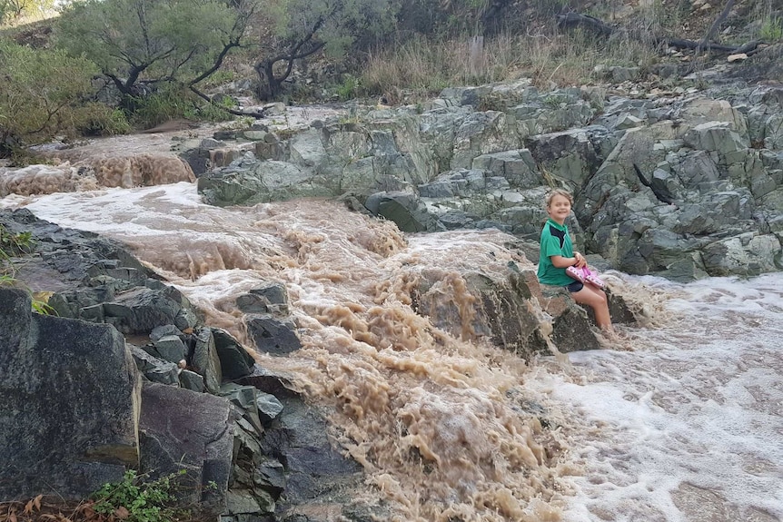 Eva Barrett sits on a rock near a flowing creek