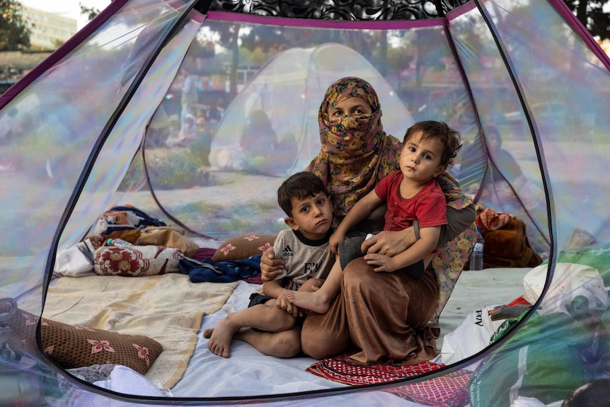 A mother and her two children sit in a tent in a makeshift camp.