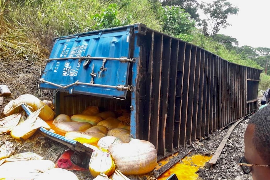 Container from a derailed freight train on the side of tracks, with the door opened and its contents across the ground.