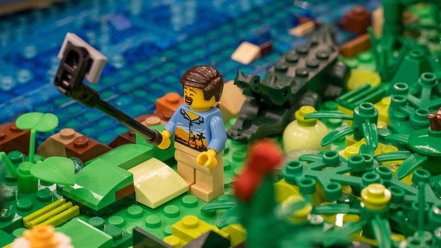 Lego figurine in tropical shirt takes a selfie with a crocodile behind him.