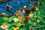 Lego figurine in tropical shirt takes a selfie with a crocodile behind him.