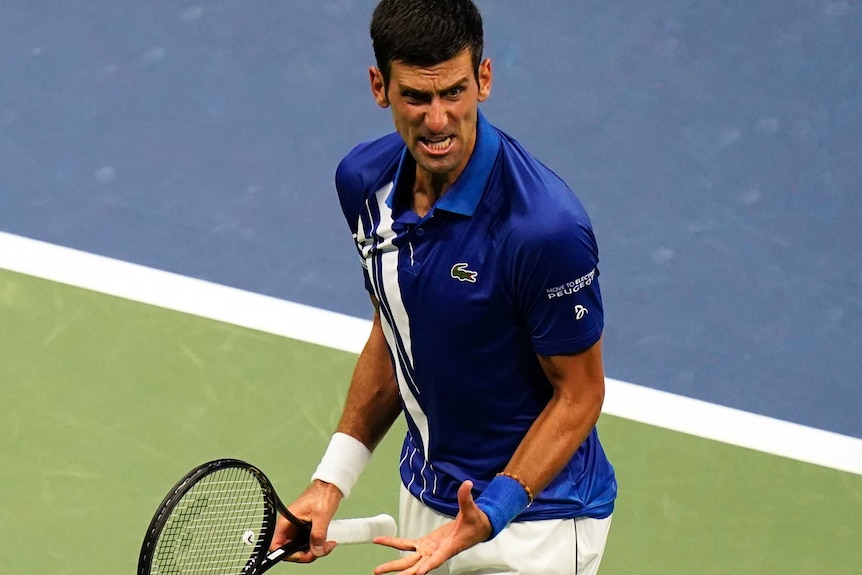 Novak Djokovic grimaces and gestures with his hand on the tennis court