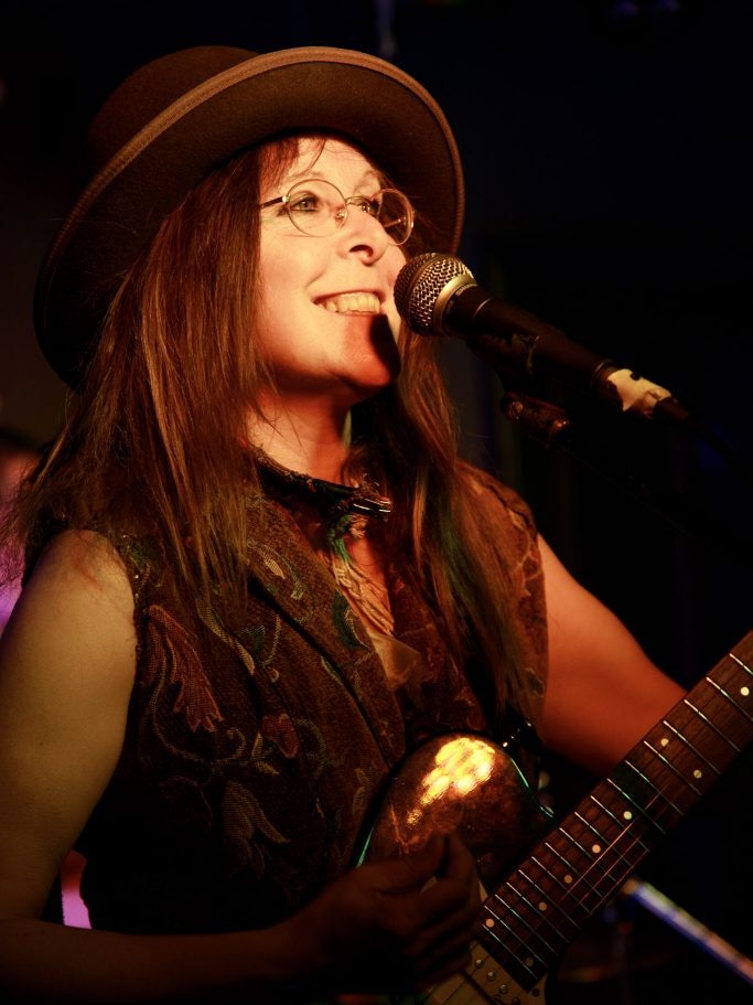 Woman in glasses and hat at microphone with electric guitar