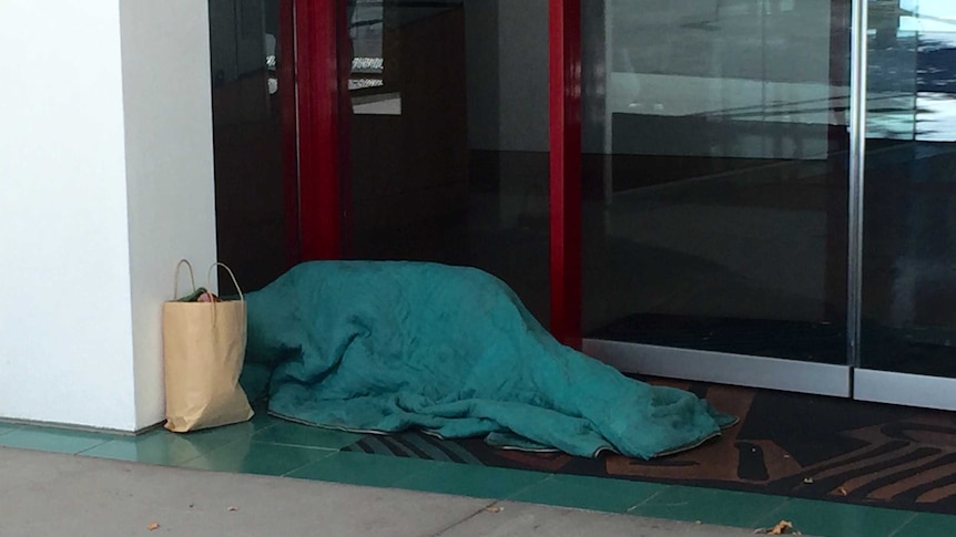 A homeless person sleeps in a doorway.