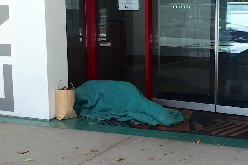A homeless person sleeps in a doorway.
