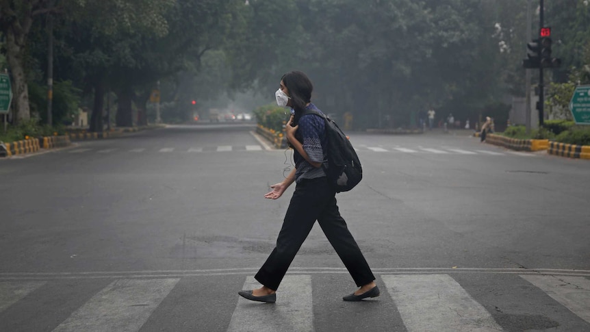 A woman wearing a face mask crosses a road