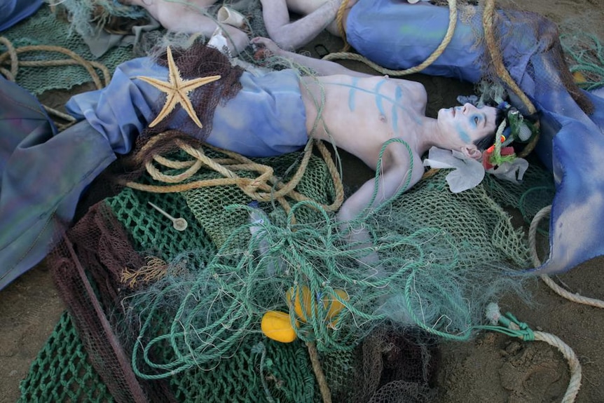 A person dressed as a mermaid tangled up in fishing nets.