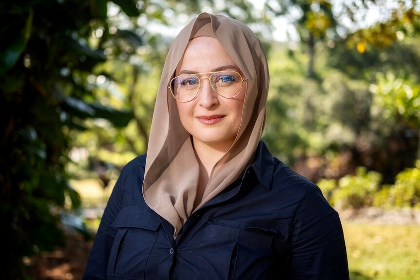 woman in a hijab stands in a park looking at camera