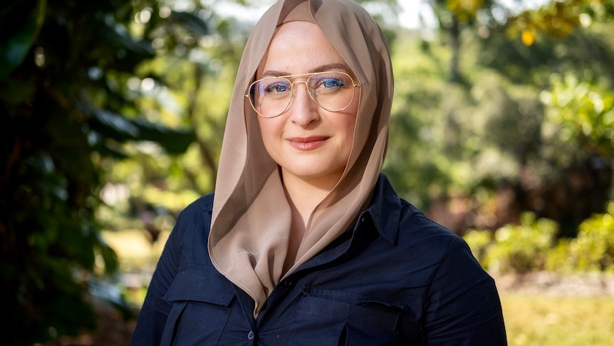 woman in a hijab stands in a park looking at camera