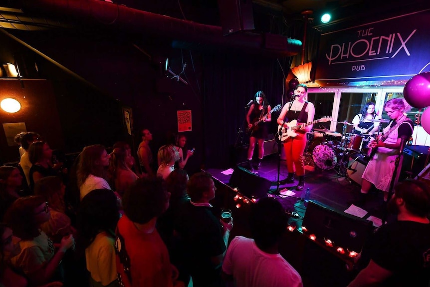 A band of four people plays on the stage, a crowd below them.