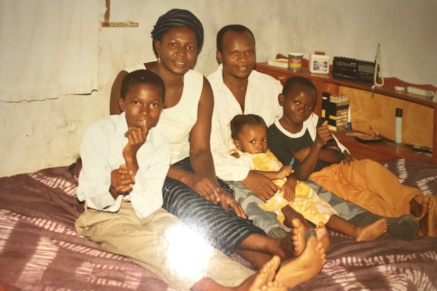 The family of Yusuf Kamara, far right, sits on a bed.