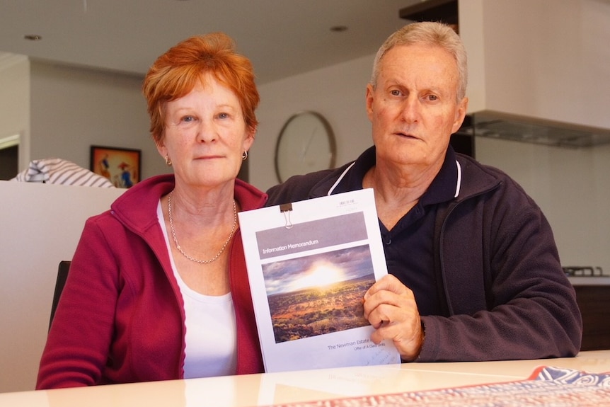 Ian and Mary Bevan sitting at their kitchen table holding a Newman Estate investment brochure