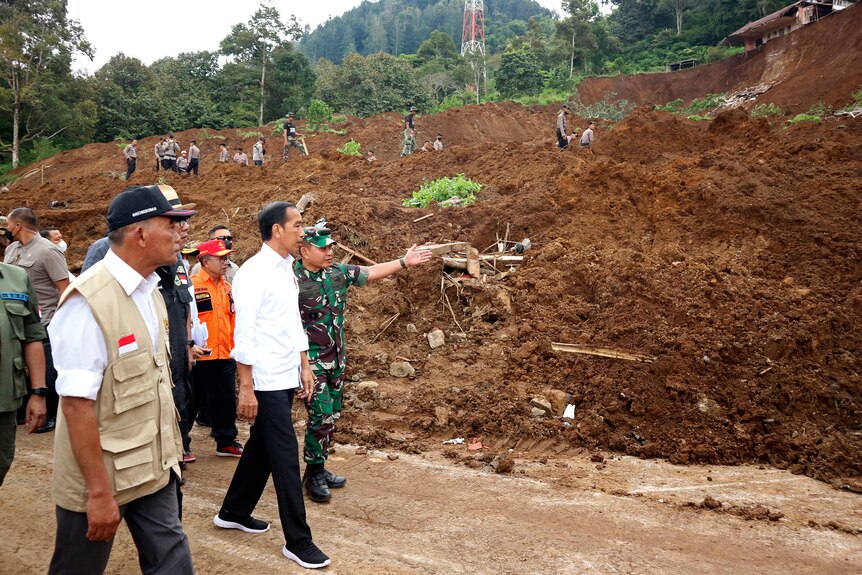 Joko Widodo walks with military officers past a landslide. 