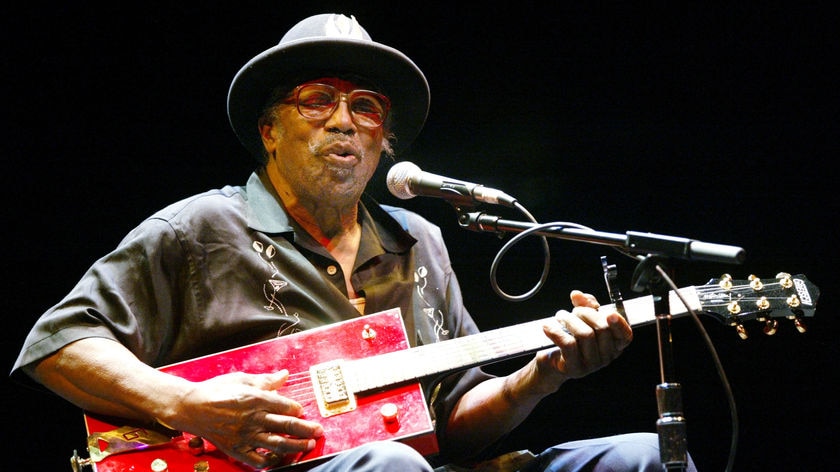 Bo Diddley plays a rectangular guitar.