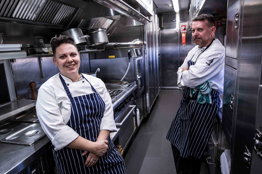Chefs wearing aprons in a stainless steel kitchen on a train