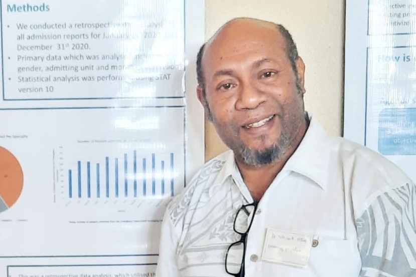 A short man of papua new guinean heritage standing in front of a map or poster in a hospital