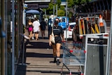 A woman wears a face mask while walking in Darwin CBD. She is wearing black shorts and a black top. It is a sunny day.